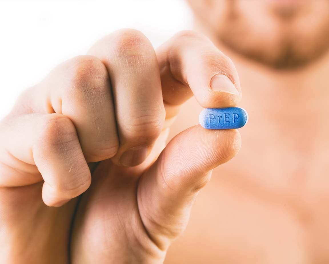 Mann hält eine blaue PrEP-Tablette zwischen Daumen und Zeigefinger – Symbol für HIV-Prävention durch präexpositionelle Prophylaxe.