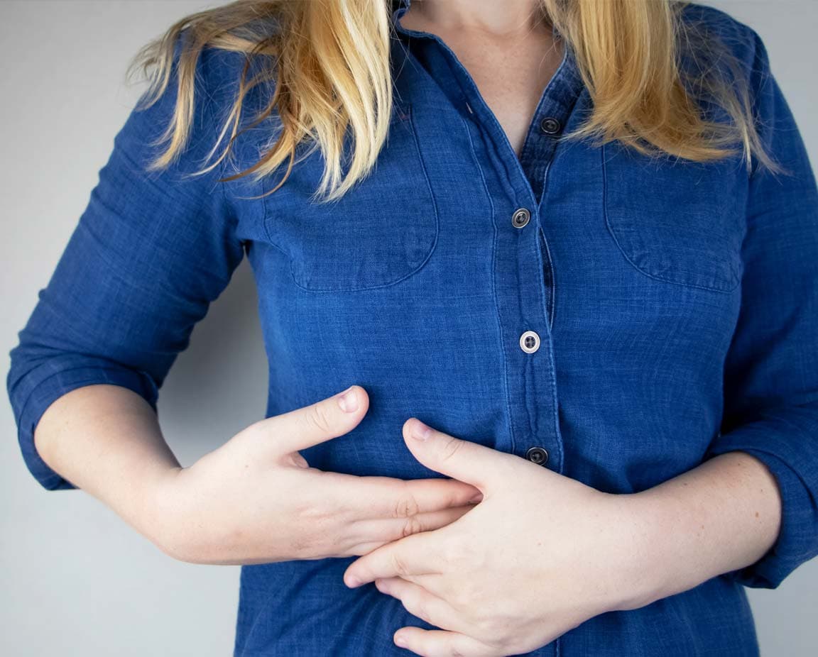 Frau hält sich den rechten Oberbauch – mögliches Anzeichen für Leberbeschwerden oder Virushepatitis wie Hepatitis B oder C.